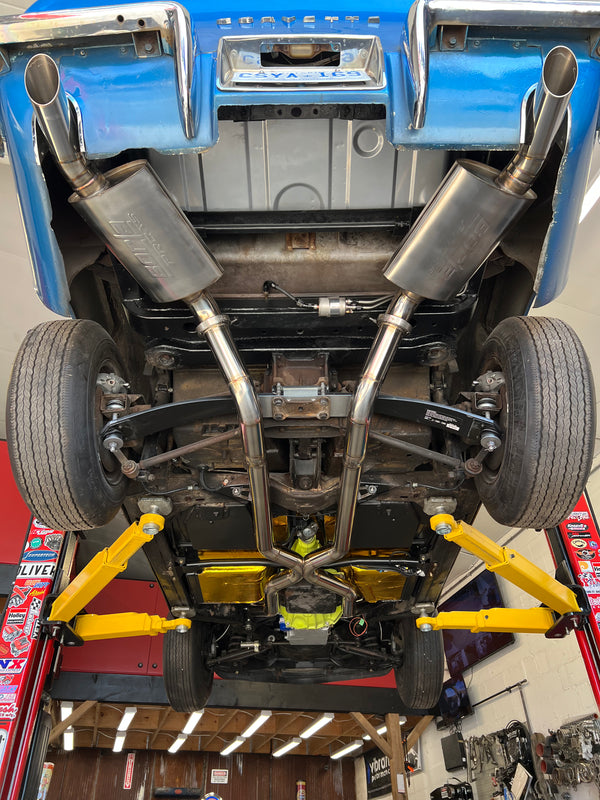 Car chassis with suspension and exhaust system on a lift in a garage.