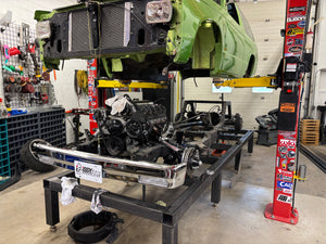 Car on a lift in a garage with visible engine and parts.