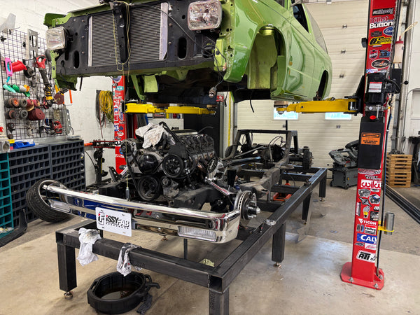 Car on a lift in a garage with visible engine and parts.