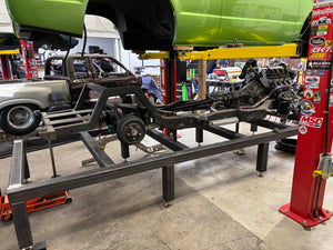 Car chassis on a lift in a garage with various tools and equipment around
