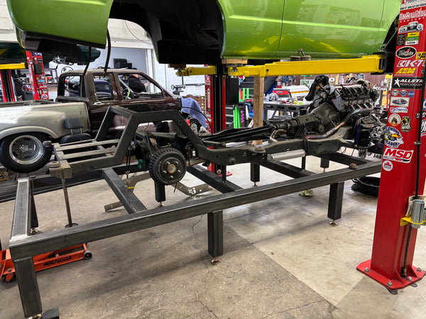 Car chassis on a lift in a garage with various tools and equipment around